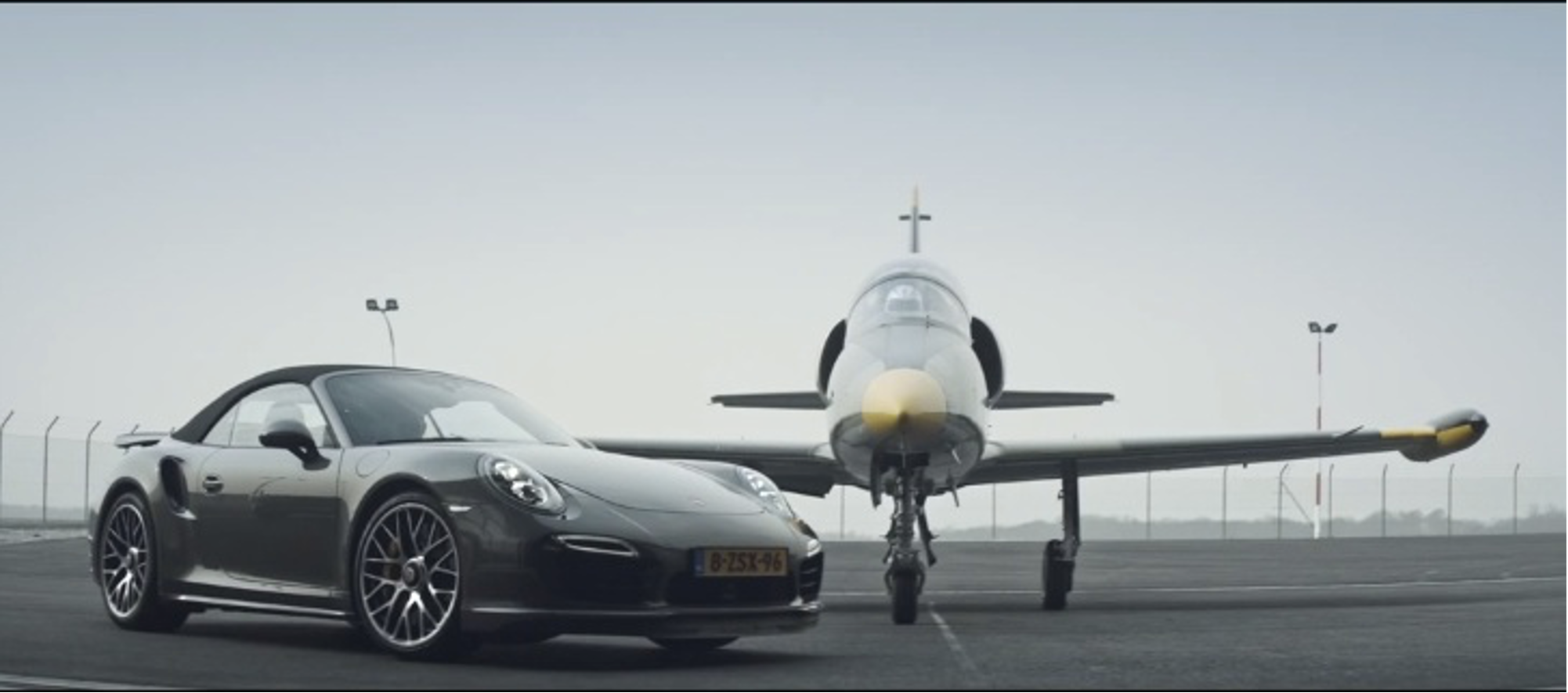 A black Porsche sports car parked on a runway in front of a fighter jet
