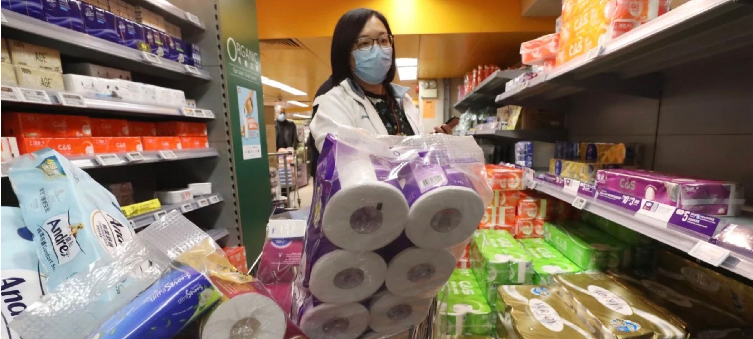A masked shopper's trolley piled high with packs of toilet paper